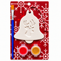 A Christmas ornament plaster painting kit on a red card with white snowflake patterns. The kit includes a white plaster bell-shaped ornament with a reindeer silhouette cutout, a blue-handled paintbrush, two small paint pots with red and yellow paint, and a red-and-white striped hanging string.
