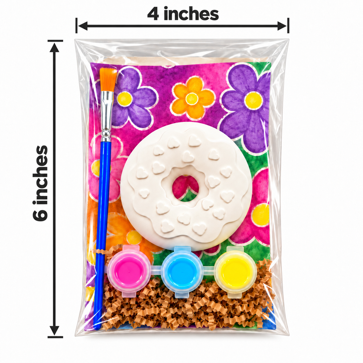 A packaged plaster paint kit shown in a clear plastic bag with dimension labels indicating 4 inches wide by 6 inches tall. The kit contains a white donut-shaped object, a blue paintbrush, three small paint pots in pink, blue, and yellow, and a colorful floral backing with brown textured pieces at the bottom.